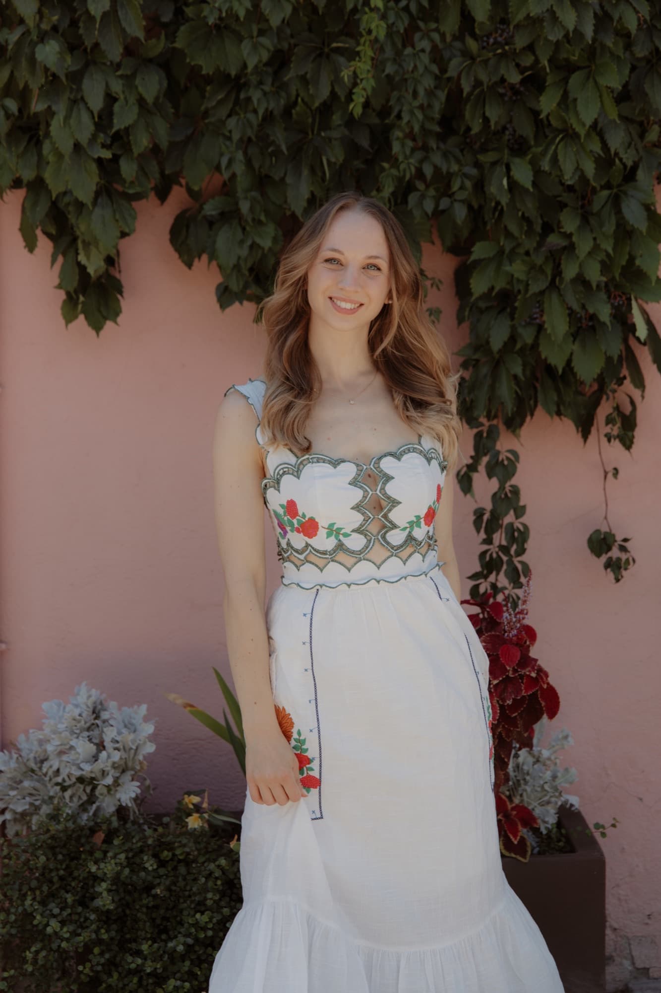 Portrait of Lara in a white dress against a pink wall